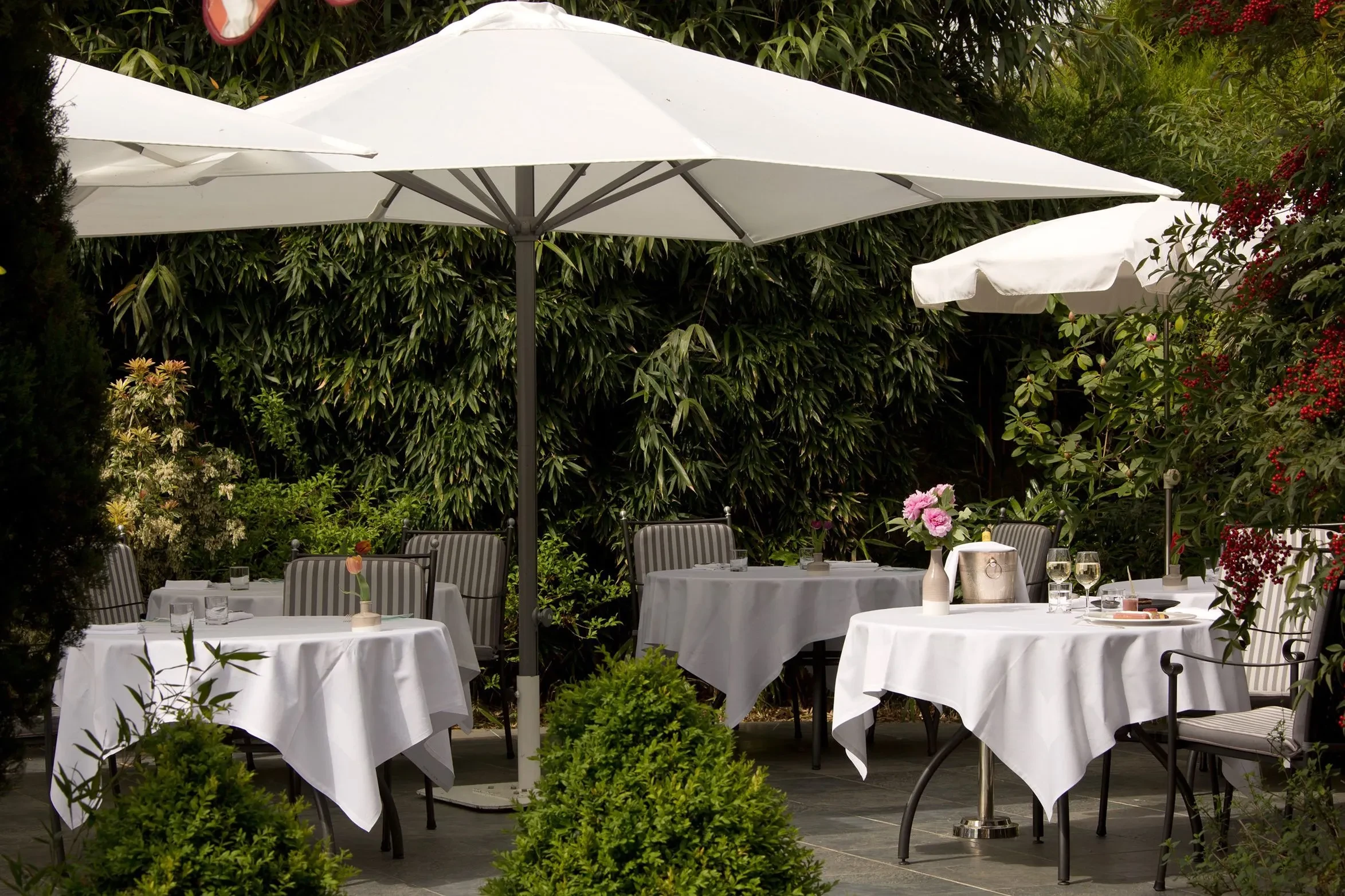 Tables extérieures sous parasols dans un jardin verdoyant. Hôtel Solesmes