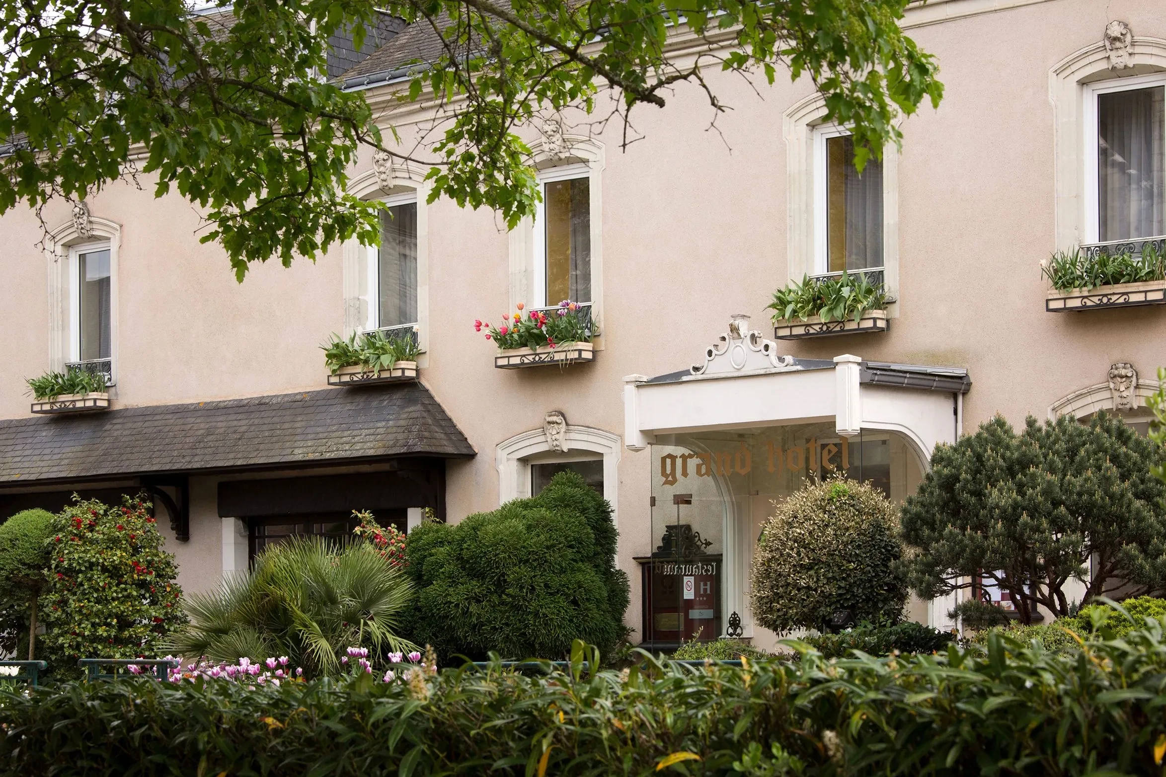 Entrée d'un Hôtel Solesmes entouré de verdure et fleurs.