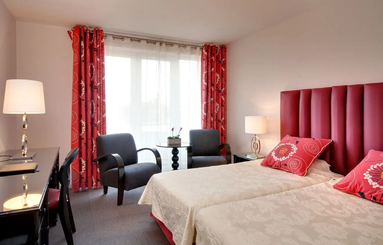 Chambre d'hôtel avec lit et fauteuils rouges.